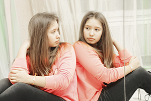 A girl facing a mirror and her reflection.