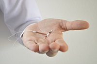 A hand holding a copper-type intrauterine device