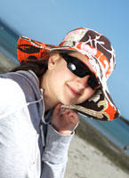 Girl on the beach with sunglasses and a hat on.