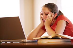 A girl sitting at a computer looking stressed.